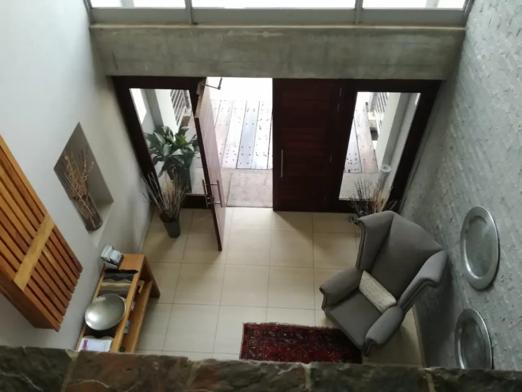 Lodge entrance and reception area with a grey armchair, decorative plants and an open wooden door.